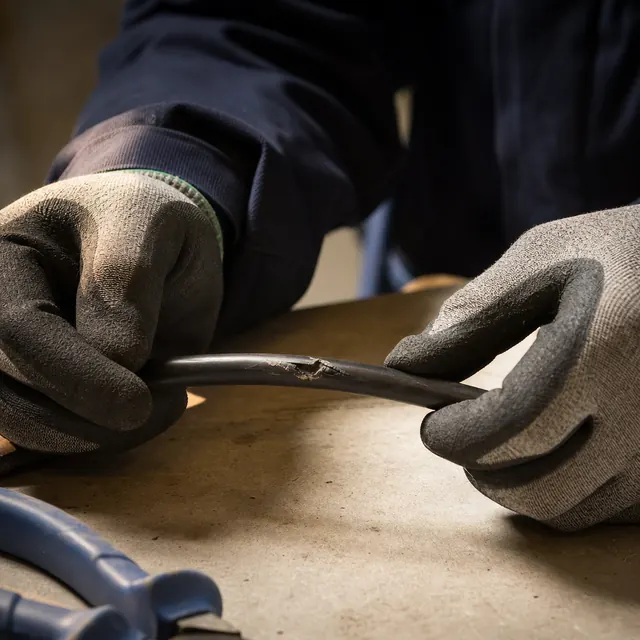 Gloved hands inspecting a damaged cable on a workbench