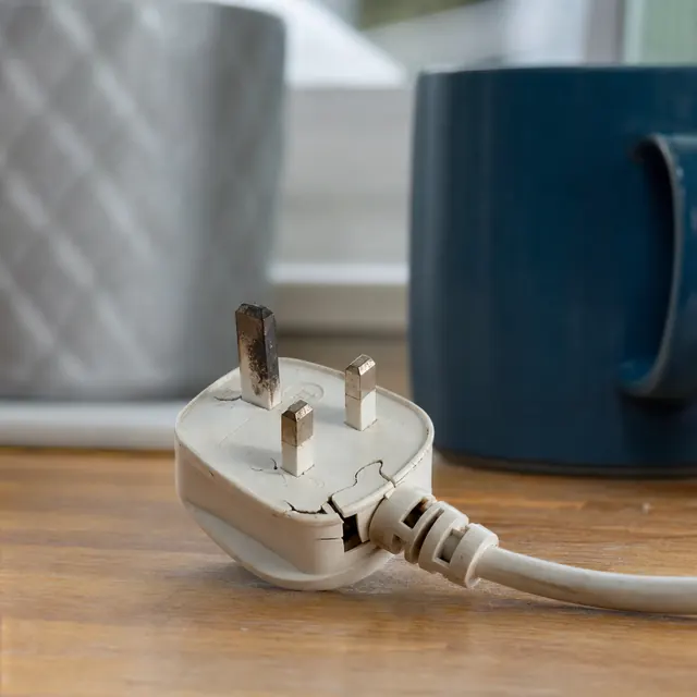 Plug with damaged pins next to a kettle on a worktop
