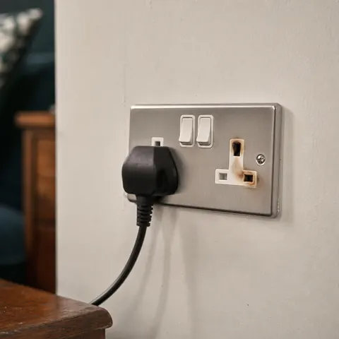 Metal double socket with a plug and switch on a pale wall